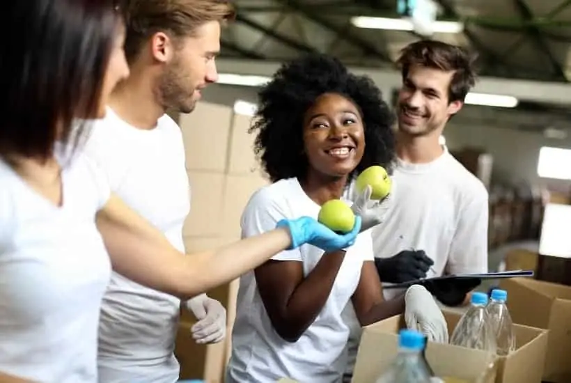 men and women wearing white shirts filling up bags of food featured image for 20 Important Bible Verses About Serving Others In Need