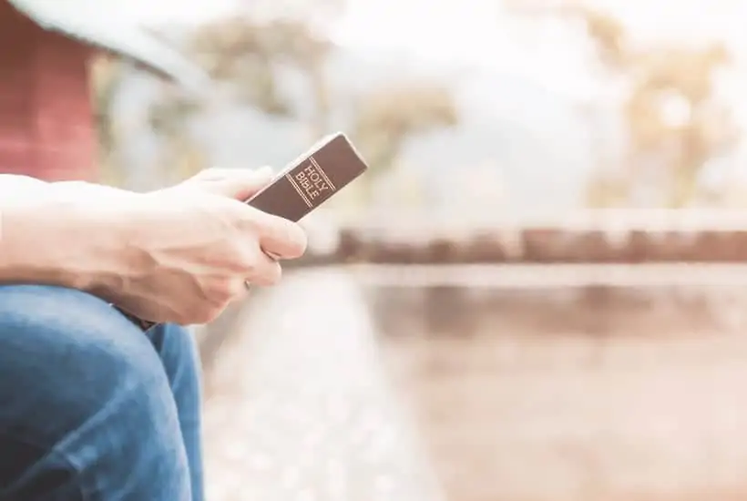 an image of a man sitting on a park park bench holding his bible featured image for Sharing Your Testimony 8 Easy Ways To Share Your Faith