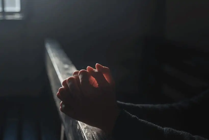 an image of a woman sitting on a church pew praying featured image for In Remembrance Of Me The Awe Inspiring Blessing of Communion