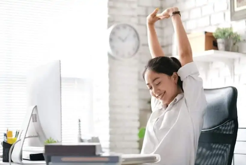 an image of a woman sitting at her desk with her arms raised and smiling. featured image for Relax God Is In Control! How Can We Rest In This Fact