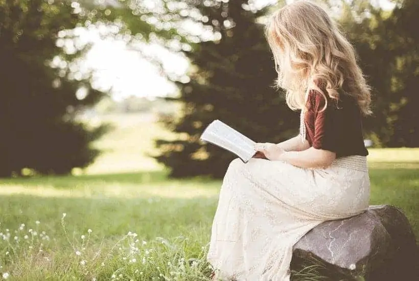 an image of woman reading the bible sitting on a rock featured image for What Does Salvation Mean? 70+ Plus Bible Verses about Salvation