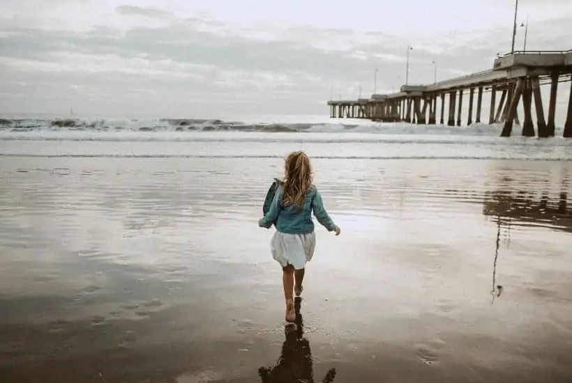 an image of a woman walking on the beach as the ocean waves are stormy with text reading Who is Your Refuge in the Storm? 3 Important Questions to Consider